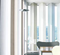 Des parois jaonaises pliantes, confectionnées sur mesure, couvrent une baie vitrée à angle droit dans un bureau.